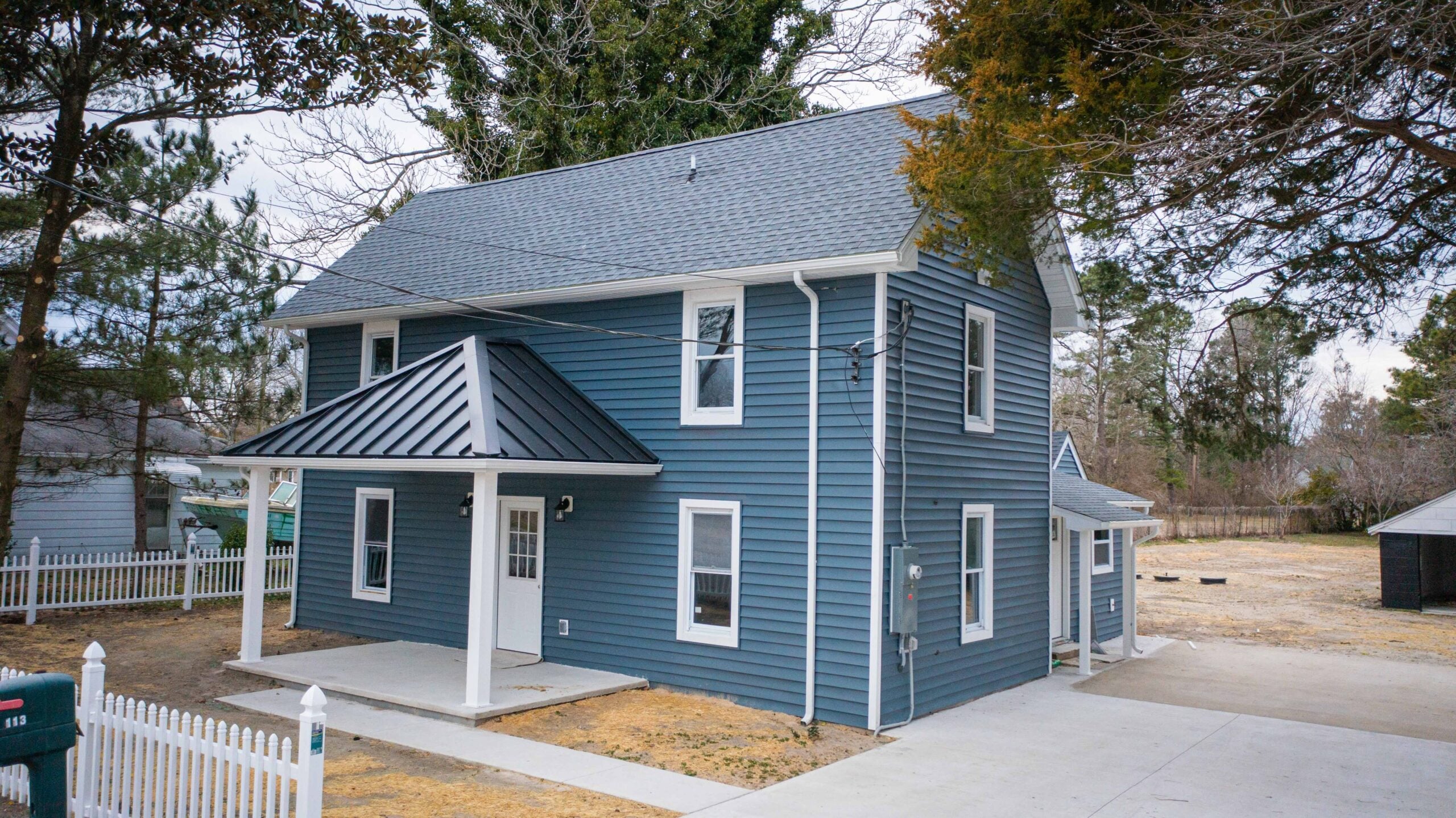 Close-up of a standing seam metal roof in a coastal residential setting, with weathered older asphalt shingle roof visible in background for visual contrast. Bright natural daylight. 
