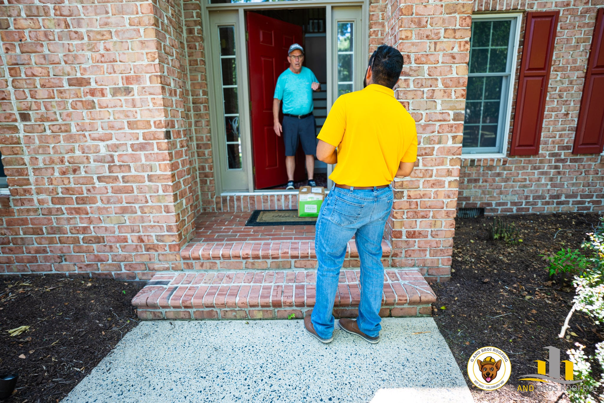 Used - Your local expert roofing company. A person in a yellow shirt delivers a package to someone at the doorway of a brick house, embodying our "Why We Don't Want to Replace Your Roof: G and Bros Roofing Perspective." The recipient stands near a green box, with red shutters and a welcome mat. Two logos are visible in the bottom right corner. G and Bros Roofing LLC Roofing Contractor Located in Salisbury MD.