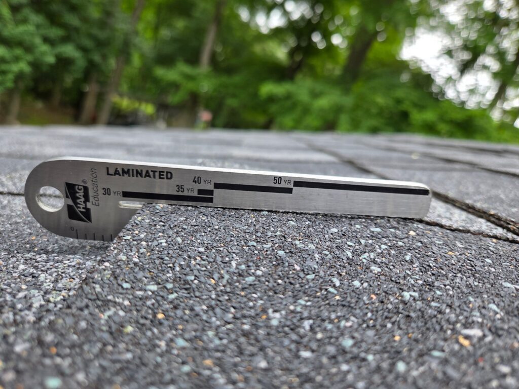Used - Close-up of a certified roofing expert using a HAAG shingle gauge to determine the age and condition of 3-tab fiberglass shingles in Maryland. Used in professional roof inspections across Salisbury, Berlin, and Ocean City.