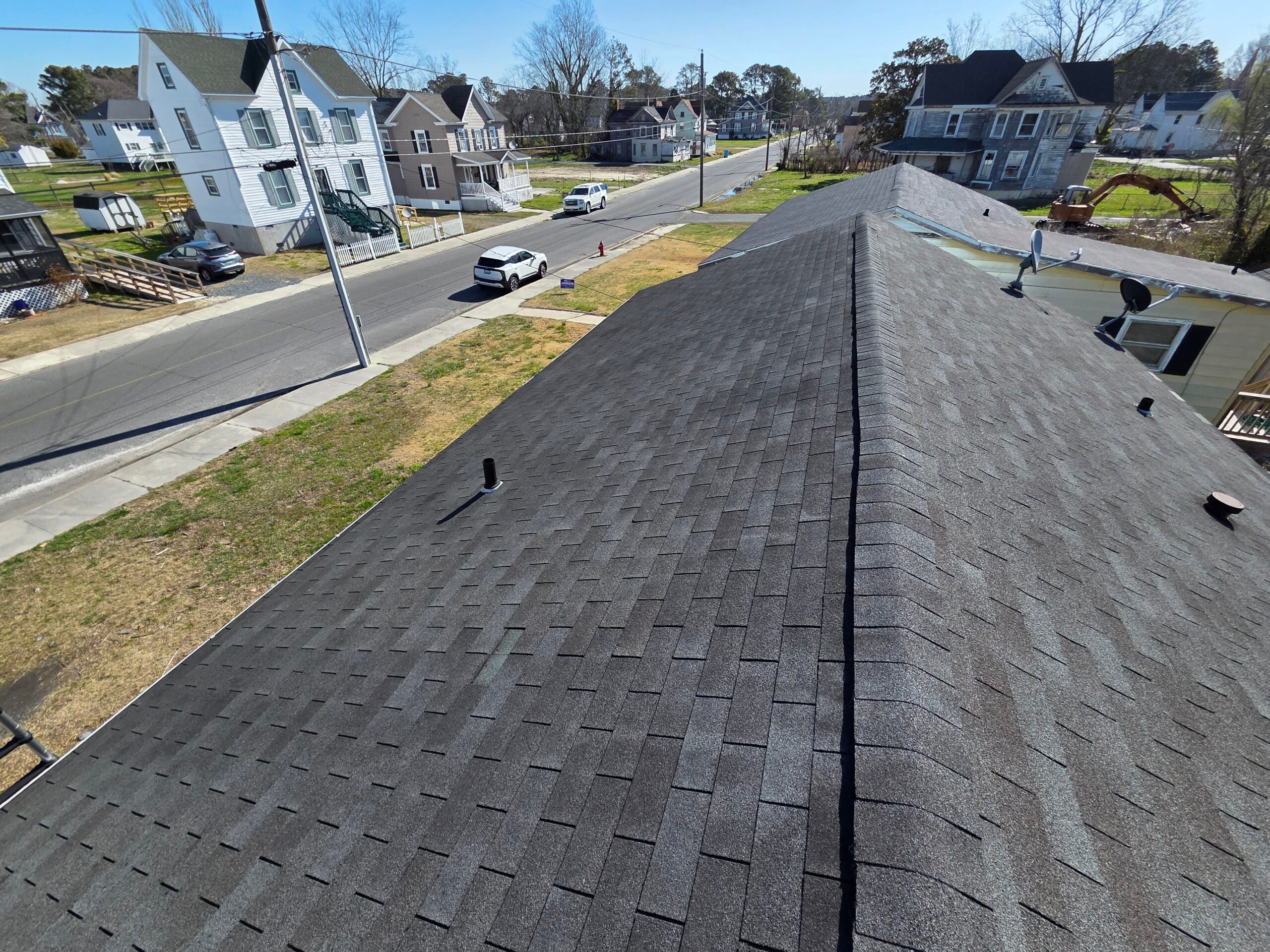 Close-up of storm-damaged asphalt shingles on a residential roof. Missing shingles and exposed underlayment visible, overcast sky after a storm, documentary-style real-damage photo