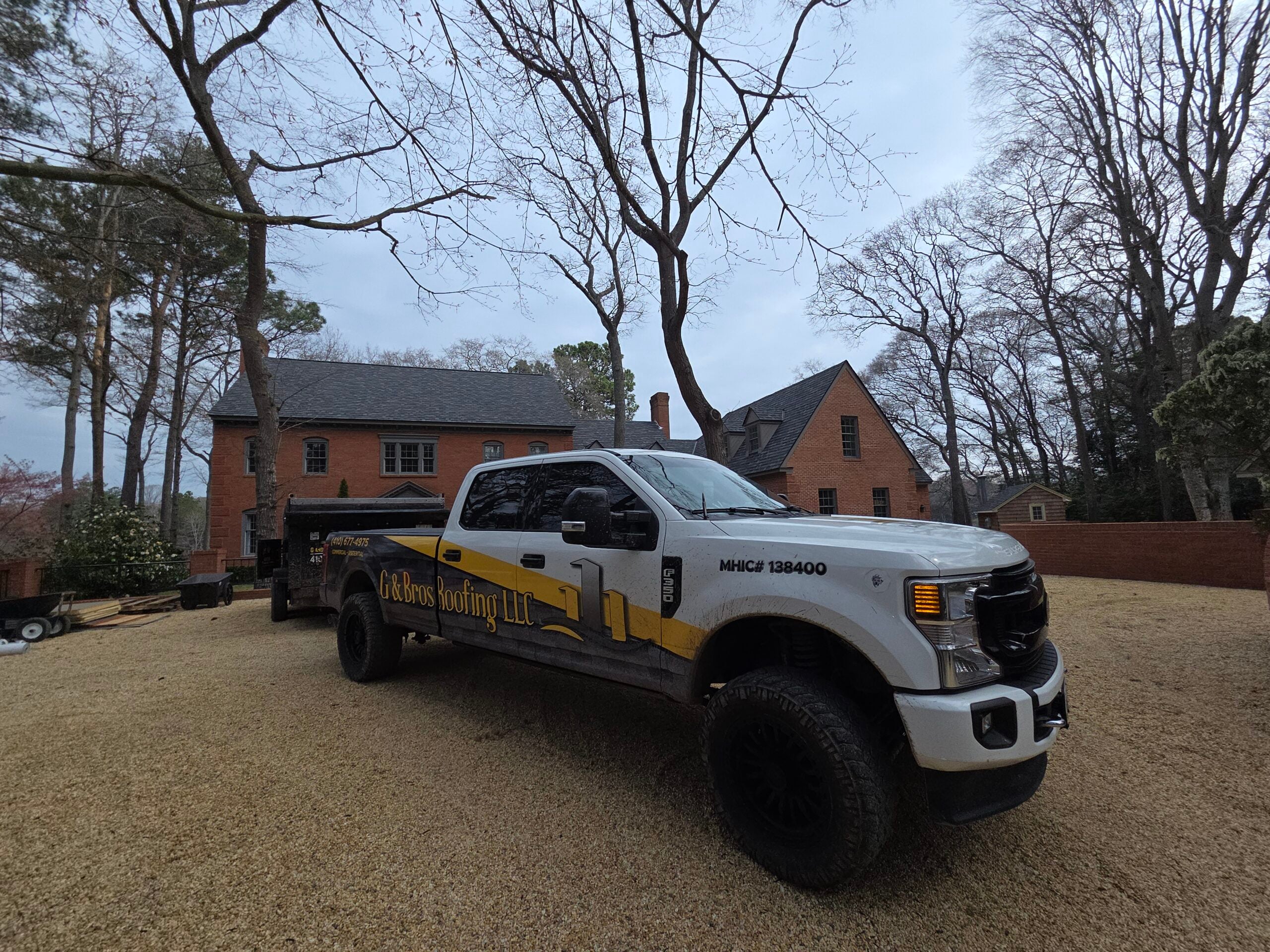 G and Bros branded truck parked in front of a completed residential roofing project on a sunny day. Crew members visible in background, Eastern Shore neighborhood setting, professional real-photo style.