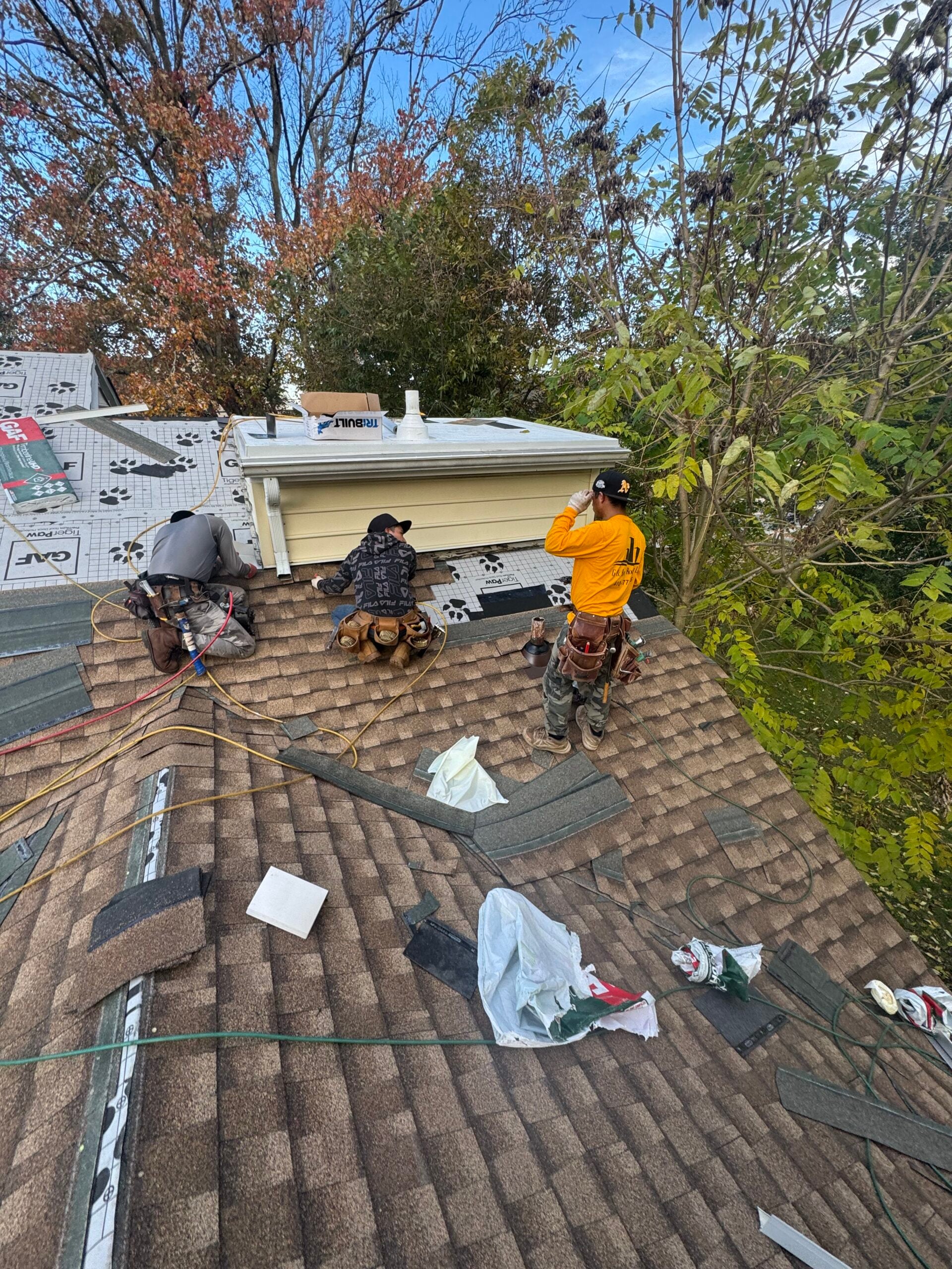 G and Bros crew member performing a close-up roof inspection on a Wicomico County home, checking flashing around a chimney or vent pipe. Bright summer daylight, Hispanic crew member. Real job photo preferred.
