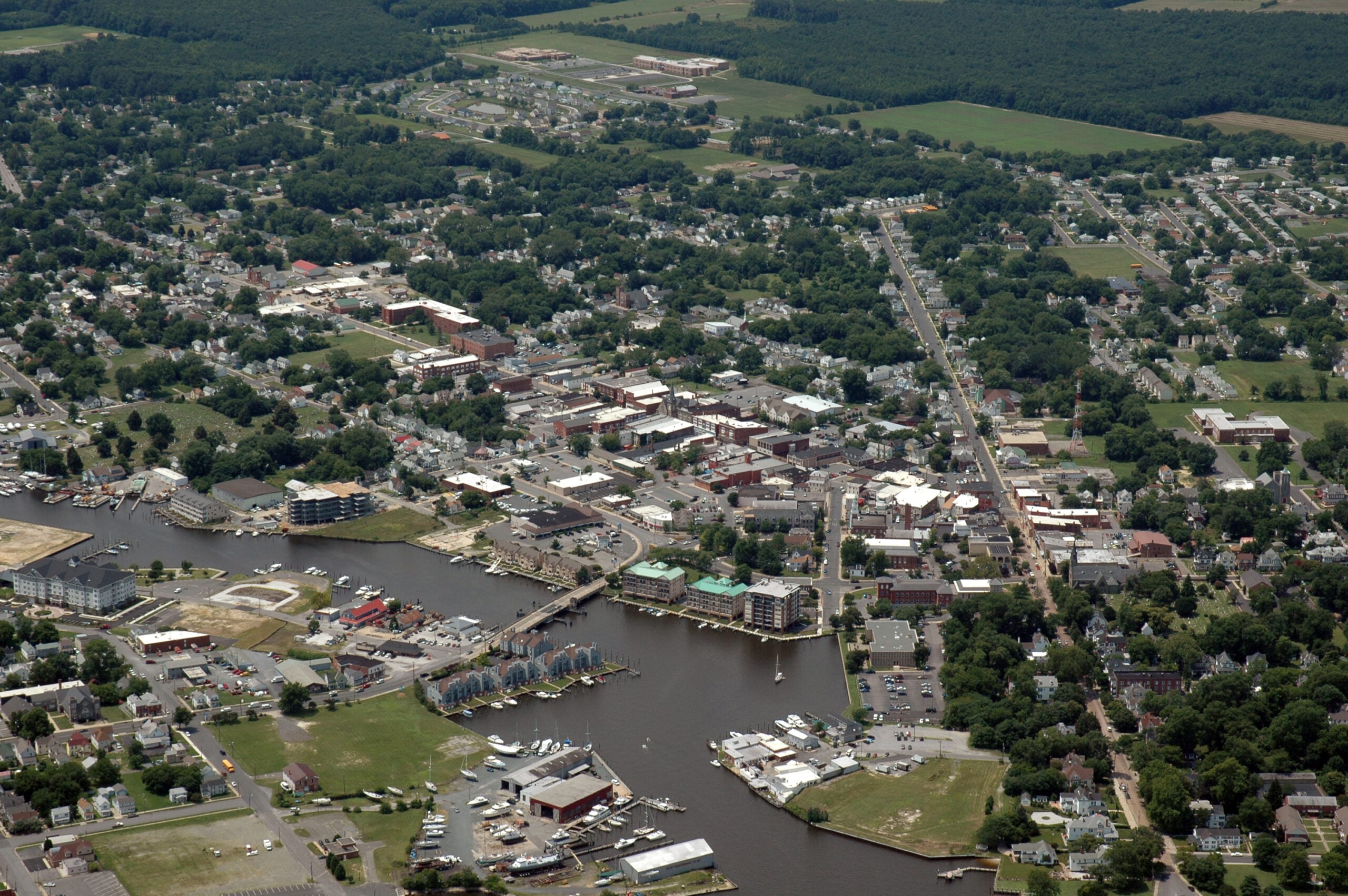 Aerial view of Cambridge, MD residential neighborhood near the Choptank River. A residential roof with missing shingles visible after a summer storm. Storm clouds breaking overhead, blue sky beginning to emerge.