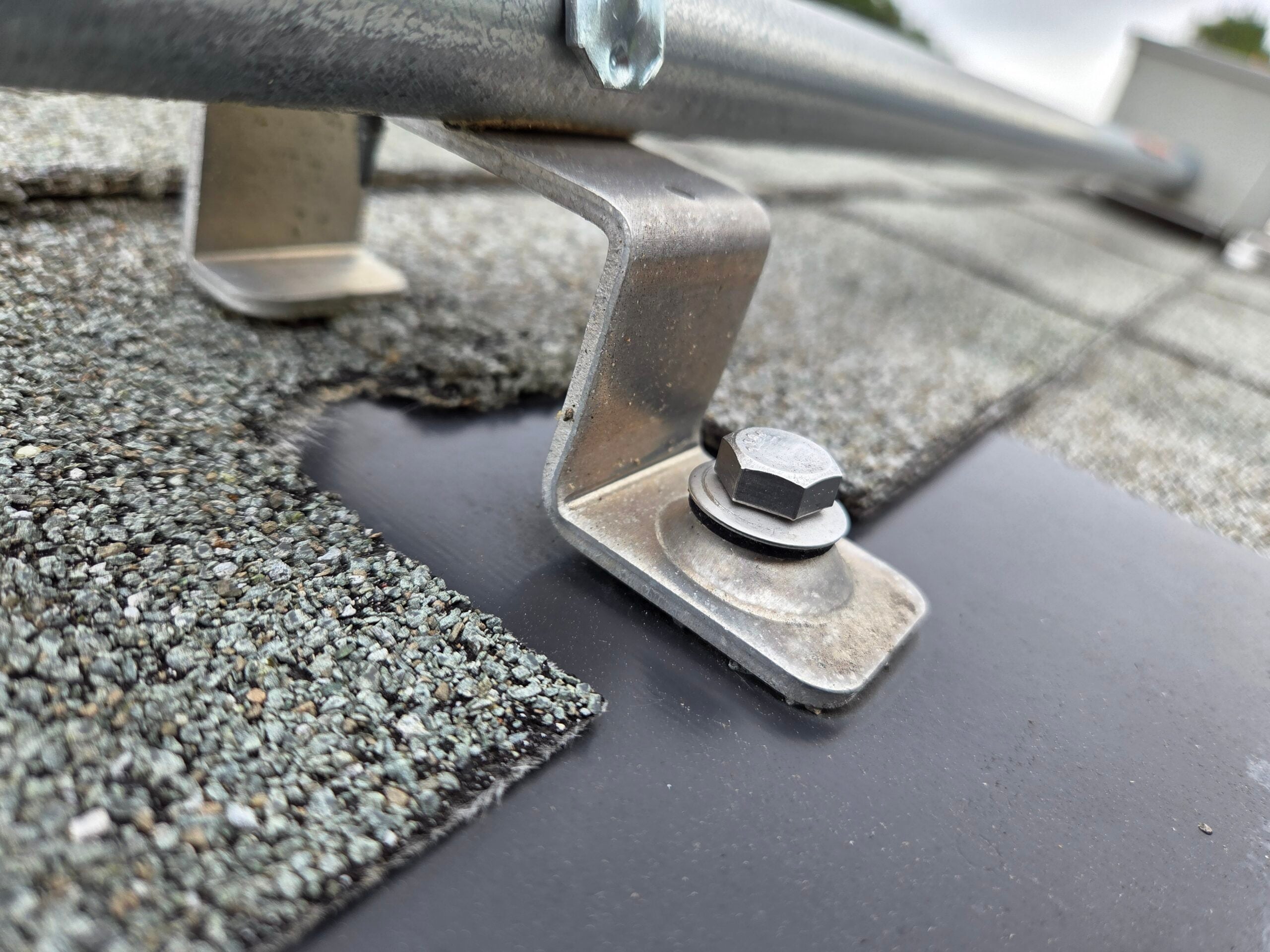 Close-up of a solar panel mounting bracket installed through asphalt shingles on a Delmarva residential roof, showing the roof penetration and flashing detail